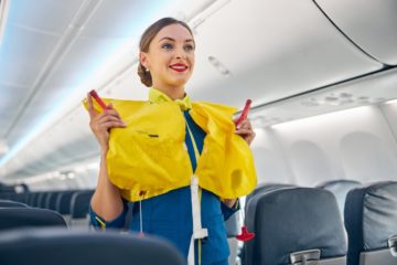 Une hôtesse de l'air passe par une procédure de sécurité avec un gilet de sauvetage dans l'allée d'un avion.
